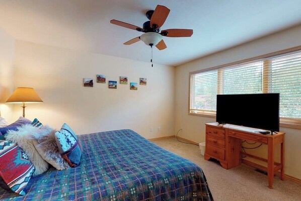 A bedroom with a bed, a desk, a ceiling fan, a TV, and a window with blinds. - Cascades Baker #2 townhome with A/C and free shuttle to the lifts (Steamboat Springs)