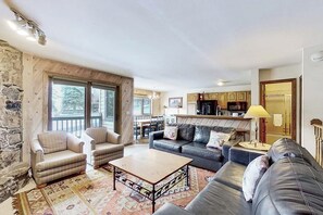 Ein Wohnzimmer mit einer Couch, Sesseln, einem Couchtisch und einer Küchenzeile mit Schränken und einem Esstisch.