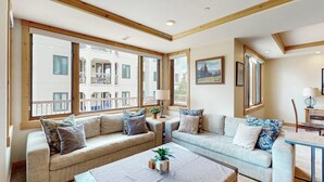 A modern living room with a sofa set, a coffee table, and large windows offering a view of a balcony. - Meadows Normandy 1 | Spacious Mountain Condo, Fireplace, Shared Pool & Hot Tub, Winter Shuttle (Steamboat Springs)