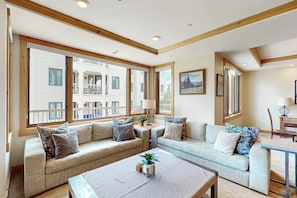 A modern living room with a sofa set, a coffee table, and large windows offering a view of a balcony. - Conveniently located condo with fully kitchen, grill, shared hot tub & pool (Steamboat Springs)