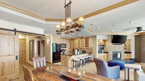 A modern kitchen with a central island, wooden cabinets, and a dining area with a large wooden table. - Meadows Normandy 1 | Spacious Mountain Condo, Fireplace, Shared Pool & Hot Tub, Winter Shuttle (Steamboat Springs)