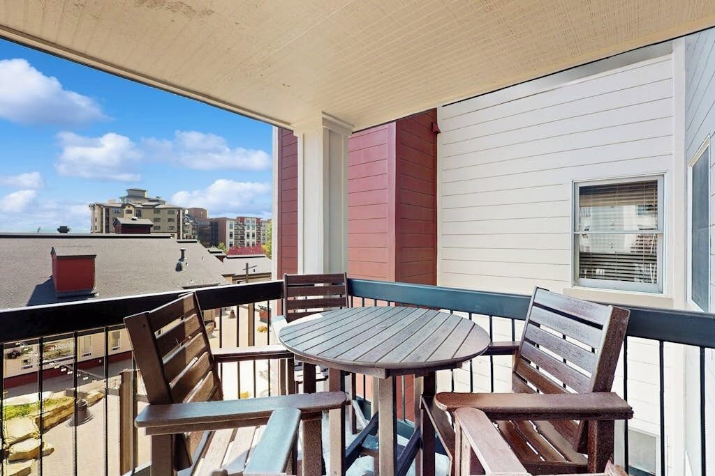 Un balcon avec une table ronde et des chaises en bois, donnant sur un panorama urbain.