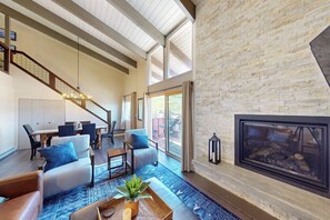 A spacious living area with a fireplace, a dining table, and a staircase. - Remodeled condo with mountain views, balcony, & hot tub access (Steamboat Springs)