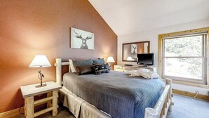 Quarto com cama, luminárias de cabeceira, televisão e janela.