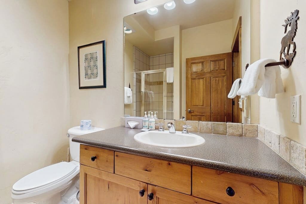 Une salle de bain comprenant des toilettes, un lavabo, un meuble en bois, un miroir et un espace douche.