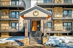 A multi-story building with a stone facade, a central entrance with a wooden door, and a balcony on the upper floors. - Ski-In/Ski-Out Condo w/ Gas Fireplace, Balcony & Shared Hot Tub (Steamboat Springs)