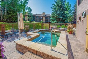 A rooftop pool with a stone deck, lounge chairs, and a wooden fence. - Ski-In/Ski-Out Condo w/ Gas Fireplace, Balcony & Shared Hot Tub (Steamboat Springs)