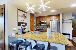 A modern kitchen with granite countertops, stainless steel appliances, and bar stools. - Beautiful Mountain Condo Near Ski Resort w/Shared Pool/Hot Tub, WiFi, AC, & W/D (Steamboat Springs)
