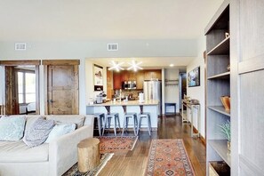 A modern living room with a sofa, a coffee table, and a kitchen area with bar stools. - Beautiful Mountain Condo Near Ski Resort w/Shared Pool/Hot Tub, WiFi, AC, & W/D (Steamboat Springs)