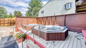 Eine Holzdielen-Terrasse mit Whirlpools, ein Holzzaun und ein Haus im Hintergrund.