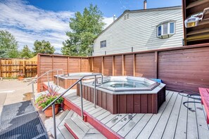 Eine Holzdielen-Terrasse mit Whirlpools, ein Holzzaun und ein Haus im Hintergrund.