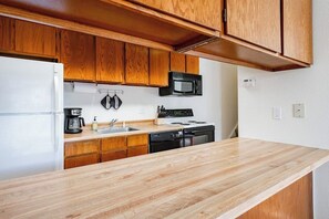 Eine Küche mit Holzausstattung, einer Mikrowelle, einem Herd, einer Spüle und einem Kühlschrank.