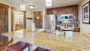Cocina con encimeras de granito, electrodomésticos de acero inoxidable, armarios de madera e iluminación colgante.