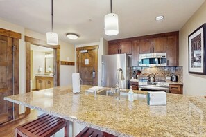 A kitchen with granite countertops, stainless steel appliances, wooden cabinets, and pendant lighting. - High-End Condo w/ WiFi, AC, Fireplace & Shared Pool/Hot Tubs/Gym - Walk to Lifts (Steamboat Springs)