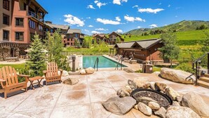Un resort con piscina, mobiliario exterior y montañas al fondo.