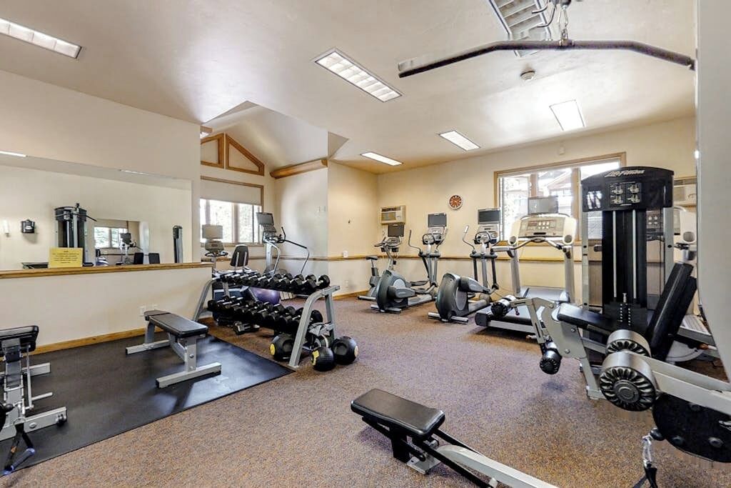 Een sportschool met diverse fitnessapparaten, een spiegel en een klok aan de muur.