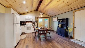 Una cocina con vigas de madera en el techo, armarios blancos, una mesa de comedor con sillas y un mueble de madera oscura.