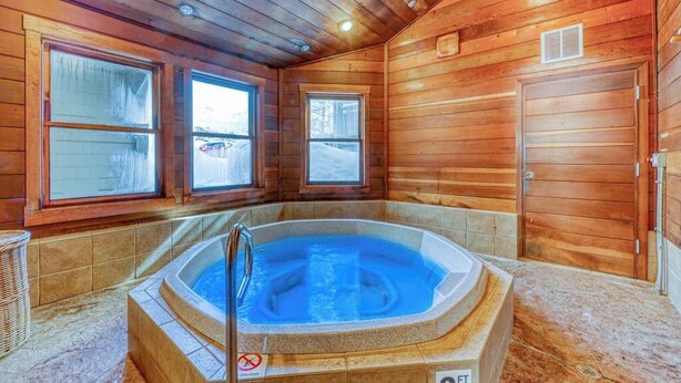Interno di una baita in legno con vasca idromassaggio, ampie finestre e una porta.