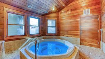 A wooden cabin interior with a hot tub, large windows, and a door.