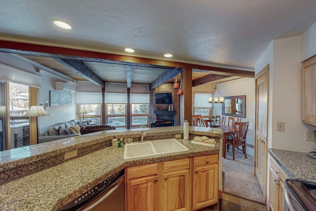 A kitchen with granite countertops, wooden cabinets, a double sink, and a dining area with chairs and a table.