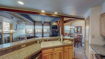 A kitchen with granite countertops, wooden cabinets, a double sink, and a dining area with chairs and a table.
