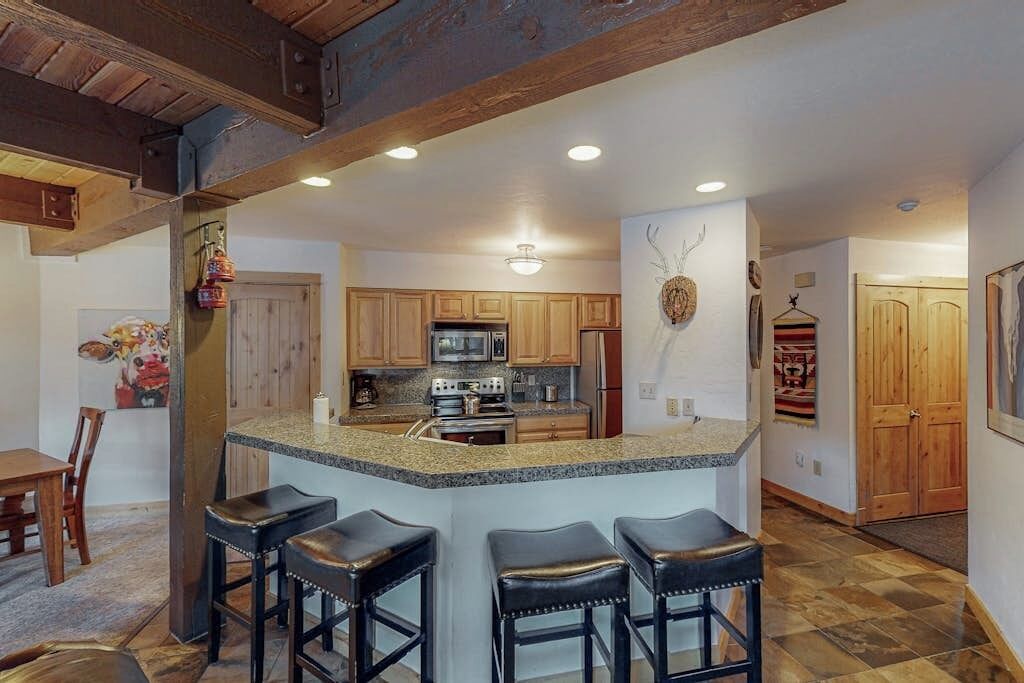 A kitchen with wooden cabinets, a granite countertop, and a central island with bar stools.