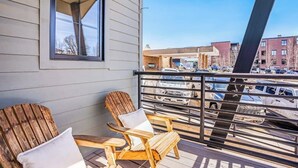 A balcony with two wooden Adirondack chairs and a window overlooking a parking lot and buildings. - Dog-friendly Alpenglow townhome with gas fireplace, fast WiFi & great location; Alpen Glow 01 (Steamboat Springs)