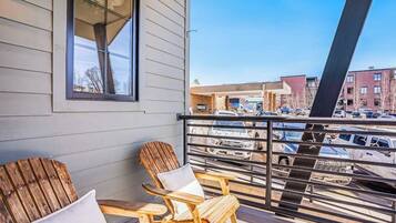 A balcony with two wooden Adirondack chairs and a window overlooking a parking lot and buildings.