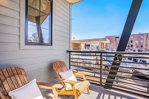 A balcony with two wooden Adirondack chairs and a window overlooking a parking lot and buildings. - Dog-friendly Alpenglow townhome with gas fireplace, fast WiFi & great location (Steamboat Springs)
