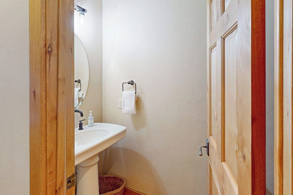 A bathroom with a wooden door, a white sink, a mirror, a towel rack, and a basket.
