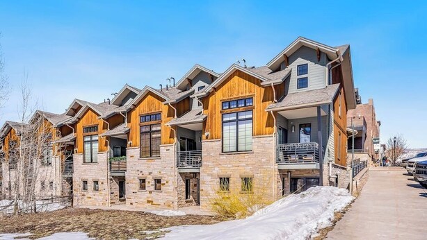 A row of modern multi-story buildings with stone facades and wooden accents, featuring balconies and large windows. - Dog-friendly Alpenglow townhome with gas fireplace, fast WiFi & great location; Alpen Glow 01 (Steamboat Springs)