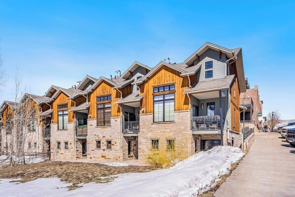 A row of modern multi-story buildings with stone facades and wooden accents, featuring balconies and large windows. - Dog-friendly Alpenglow townhome with gas fireplace, fast WiFi & great location (Steamboat Springs)