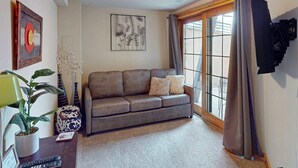 A living room with a sofa, a potted plant, a lamp, and artwork on the walls. - Dog-friendly Alpenglow townhome with gas fireplace, fast WiFi & great location; Alpen Glow 01 (Steamboat Springs)