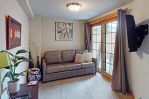 A living room with a sofa, a potted plant, a lamp, and artwork on the walls. - Dog-friendly Alpenglow townhome with gas fireplace, fast WiFi & great location (Steamboat Springs)