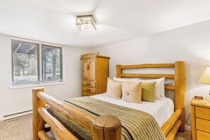 Ein Schlafzimmer mit einem hölzernen Bett, einem Nachttisch, einem Holzschrank und einem Fenster mit Jalousien.