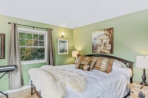 Ein Schlafzimmer mit Bett, Fenster mit Vorhängen, einer Lampe und einem Gemälde an der Wand.