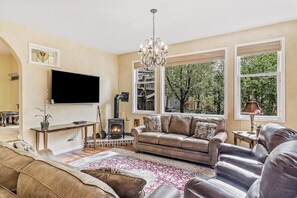 Ein Wohnzimmer mit Kamin, Sofa, Fernseher und großen Fenstern.