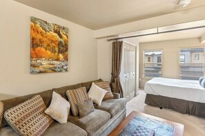A room with a sofa, a bed, a painting, and a window with blinds. - Spacious Steamboat studio near skiing with pool, hot tubs, gym & W/D (Steamboat Springs)