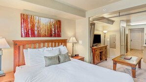 Een hotelkamer met een groot bed, een houten hoofdeinde, een schilderij aan de muur, een bureau met een lamp en een televisie.