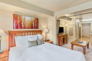 A hotel room with a large bed, a wooden headboard, a painting on the wall, a desk with a lamp, and a television. - Spacious Steamboat studio near skiing with pool, hot tubs, gym & W/D (Steamboat Springs)