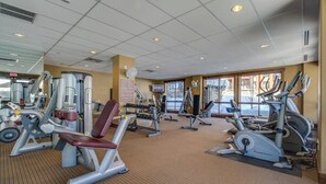 Een fitnessruimte met diverse trainingsapparaten, een televisie en grote ramen.
