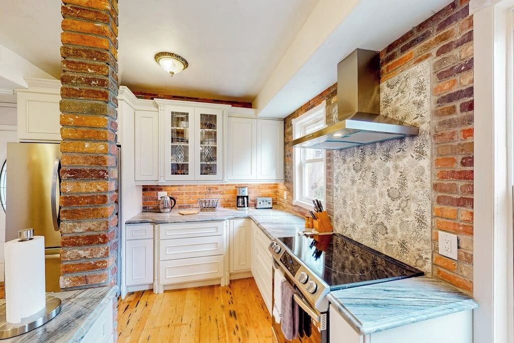 A kitchen with white cabinets, a brick accent wall, a stove, and a window.
