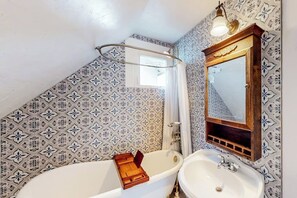 A bathroom with a freestanding bathtub, a sink, a mirror, and patterned tiles. - Restored downtown home with front porch, mountain views, & washer/dryer (Steamboat Springs)