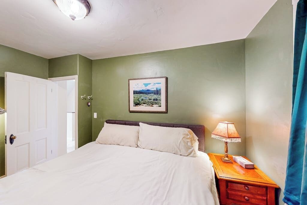 Ein Schlafzimmer mit Bett, Nachttisch, Lampe, gerahmtem Bild an der Wand und einer Tür.