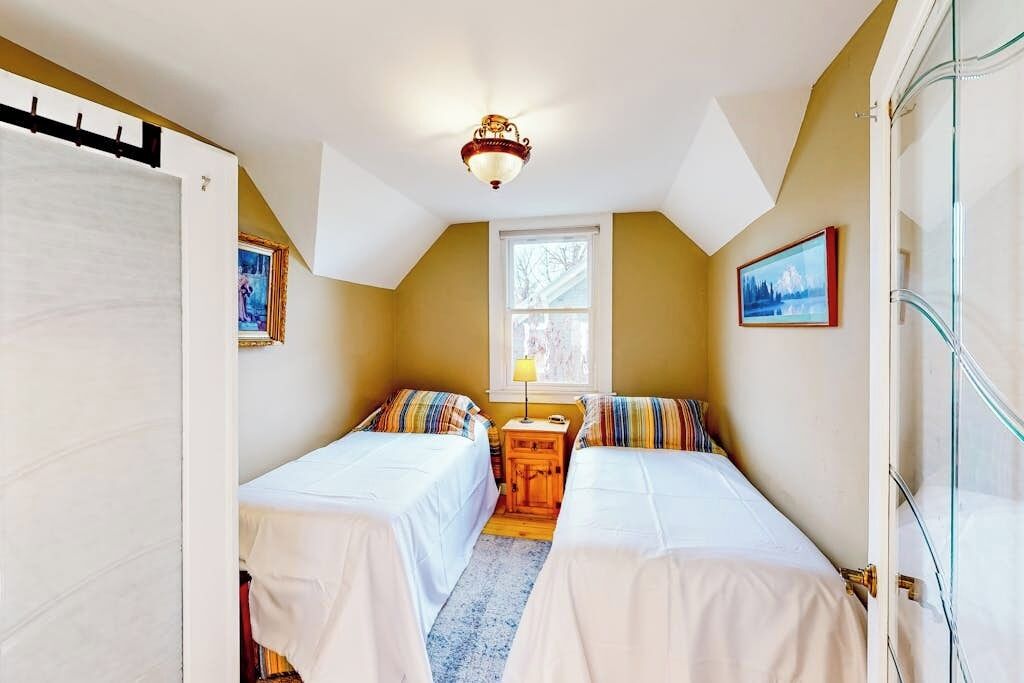 A small bedroom with two beds, a window, a ceiling light, and a door.