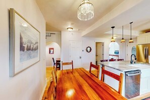 A spacious kitchen with wooden flooring, a dining area with a wooden table and chairs, a chandelier, and a refrigerator. - Restored downtown home with front porch, mountain views, & washer/dryer (Steamboat Springs)