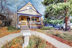 A two-story building with a porch, a front door, and a small staircase leading to the entrance. - Restored downtown home with front porch, mountain views, & washer/dryer (Steamboat Springs)