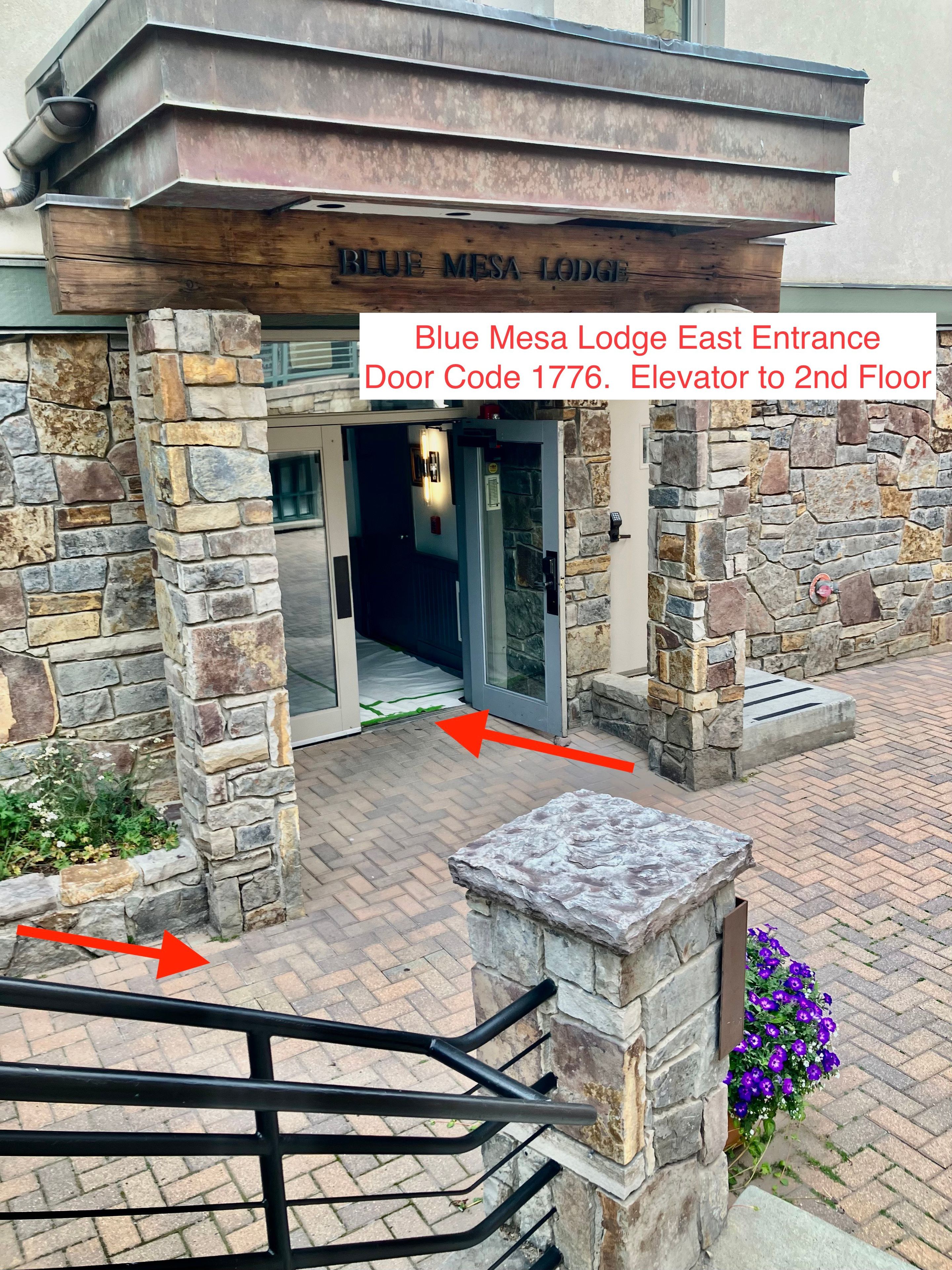 La entrada del Blue Mesa Lodge East, con fachada de piedra, techo metálico y una puerta marcada con el código 1776.
