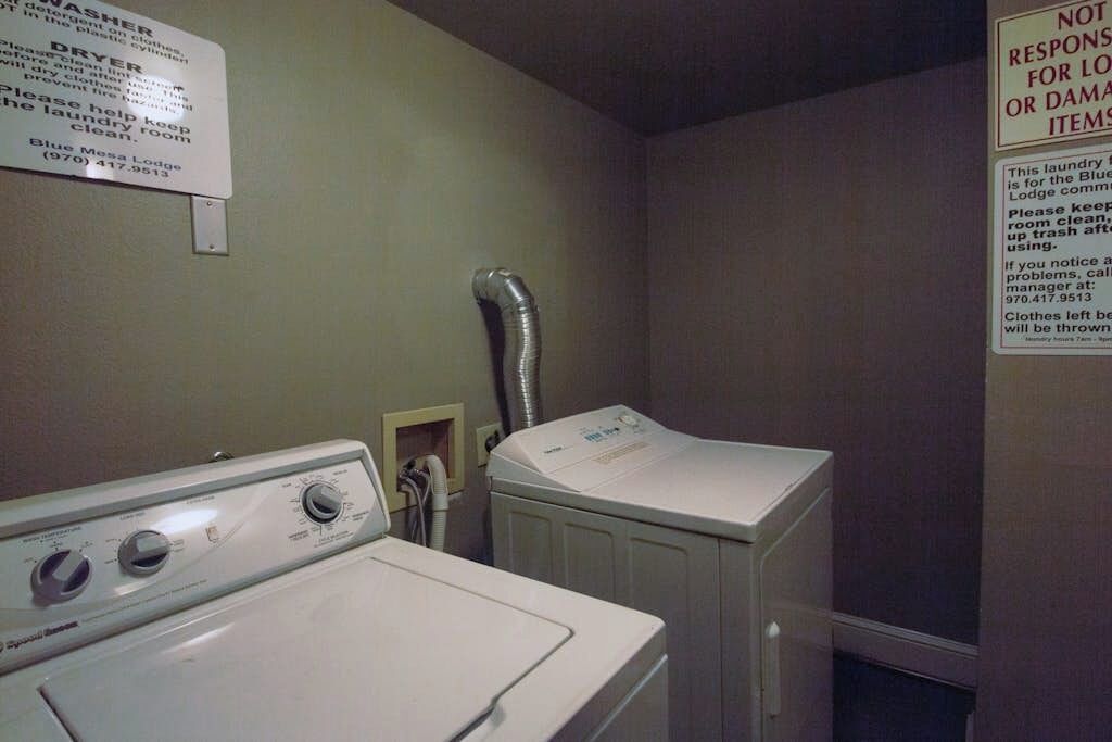 Un espace buanderie équipé de deux machines à laver, d’un sèche-linge et d’un panneau indiquant les règles à respecter pour l’utilisation de la buanderie.