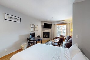 A hotel room with a bed, a desk, a chair, a sofa, a fireplace, and a TV. - Stunning ski studio with pool, hot tub, firepit & mountain views - walk to lifts (Steamboat Springs)